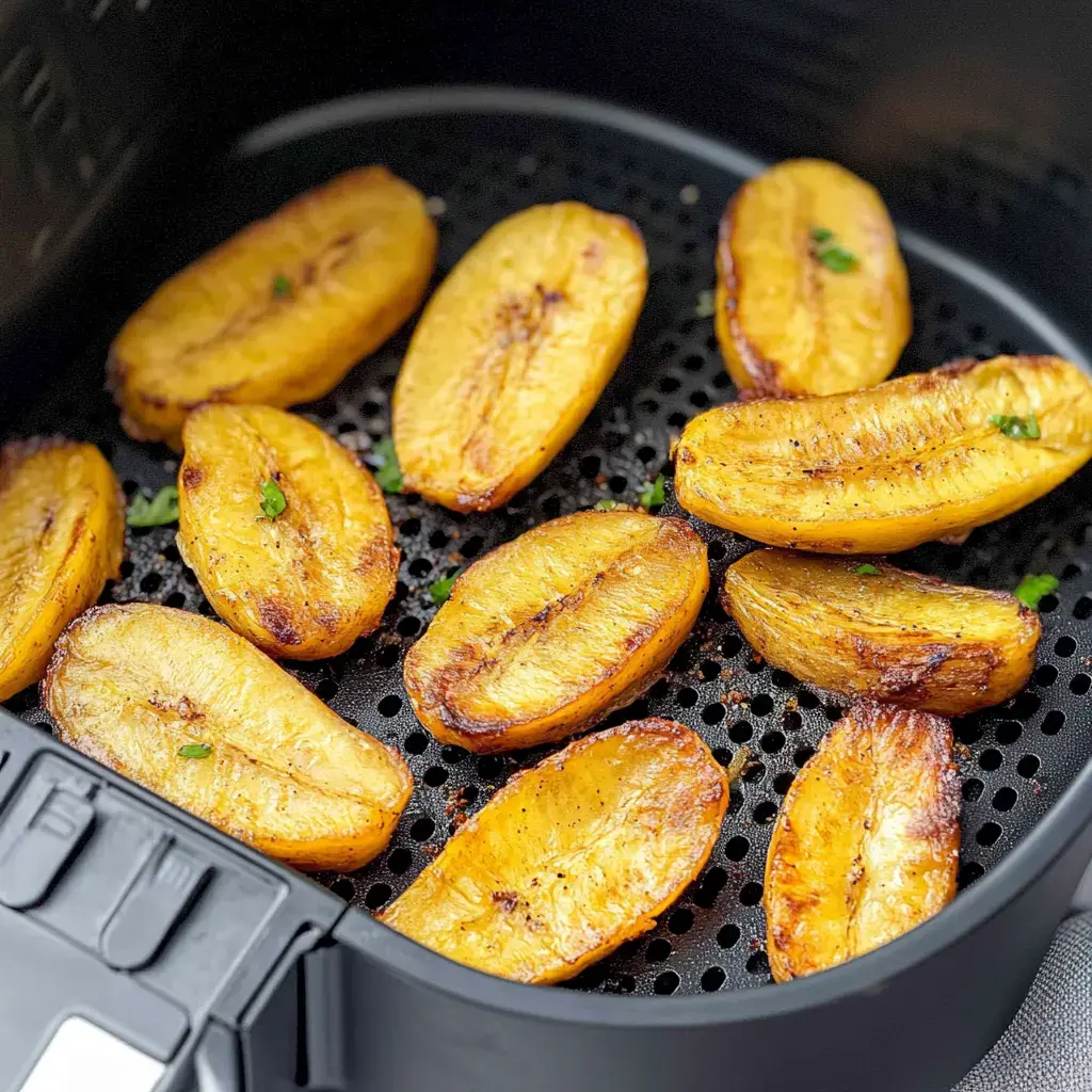Air-fried golden plantains arranged neatly in a black basket with small flecks of green seasoning on top.