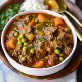 Warm bowl of stew with beef, carrots, and peas on display.