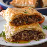 Two flaky pastries stuffed with flavorful meat and veggies, served on a white plate.