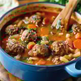 A steaming bowl filled with juicy meatballs, veggies, and tomato broth.