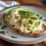 Sandwich topped with eggs, avocado, and chives.