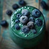 A glass of spirulina blend with blueberries on top.