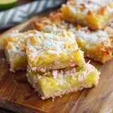 A wooden cutting board holding a slice of coconut dessert with pineapple.