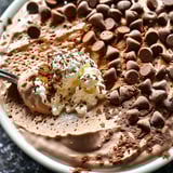 A bowl of creamy chocolate dessert topped with chocolate chips.